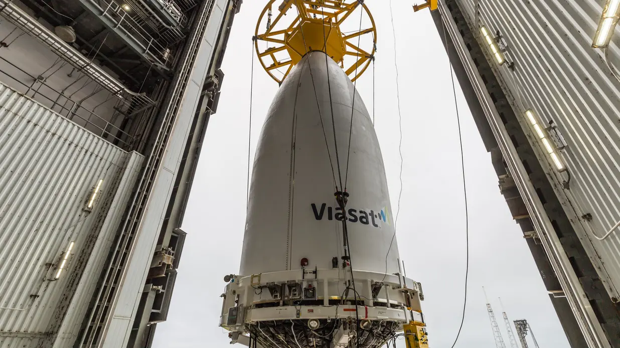 یک پوشش بار مخروطی سفید توسط جرثقیل در داخل آشیانه بلند می‌شود