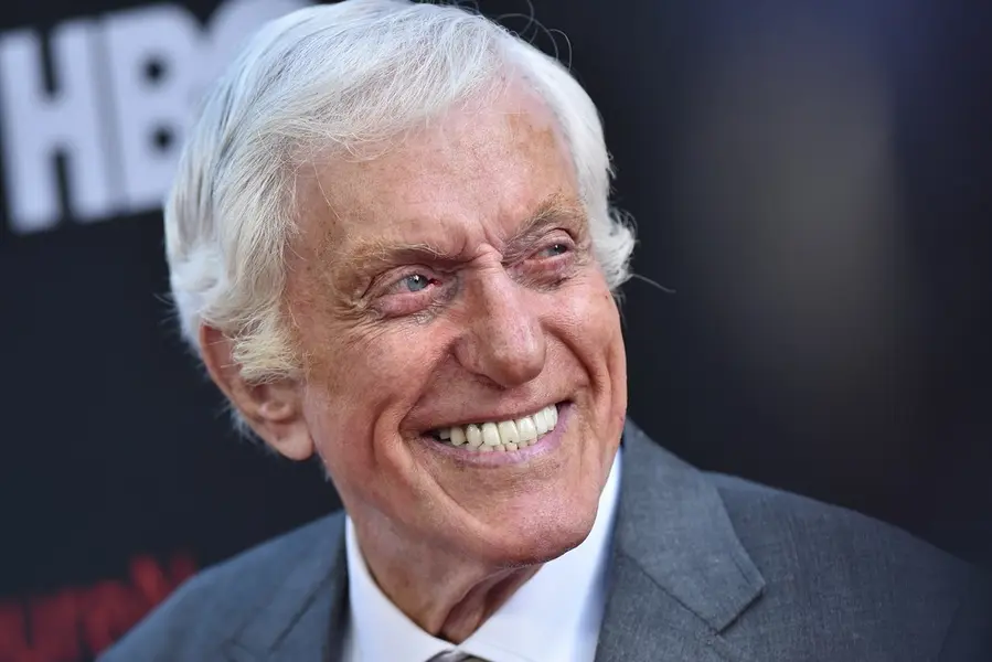 تصویر نزدیک از دیک ون دیِک در کت خاکستری و با لبخند پهن.