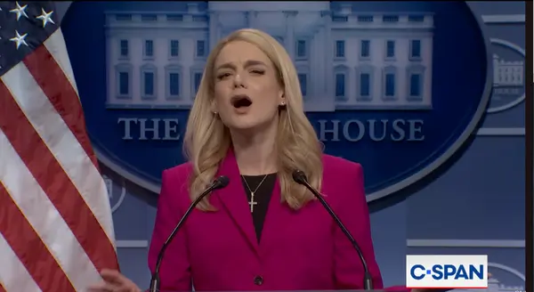 یک زن بلوند با ژاکت صورتی روشن و گردنبند صلیبی بزرگ به‌صورت پرشور برای مطبوعات کاخ سفید سخن می‌گوید.