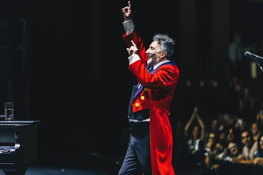 خواننده‌ای روی صحنه مقابل جمعیتی که دست خود را بلند کرده است.